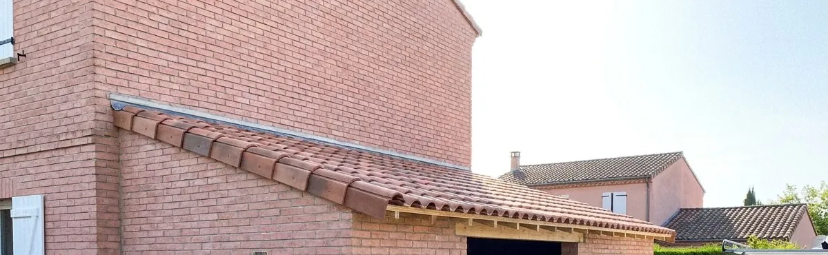 Toiture d’appentis refaite en tuiles canal neuves contre une maison en brique rose, lotissement du nord-est toulousain